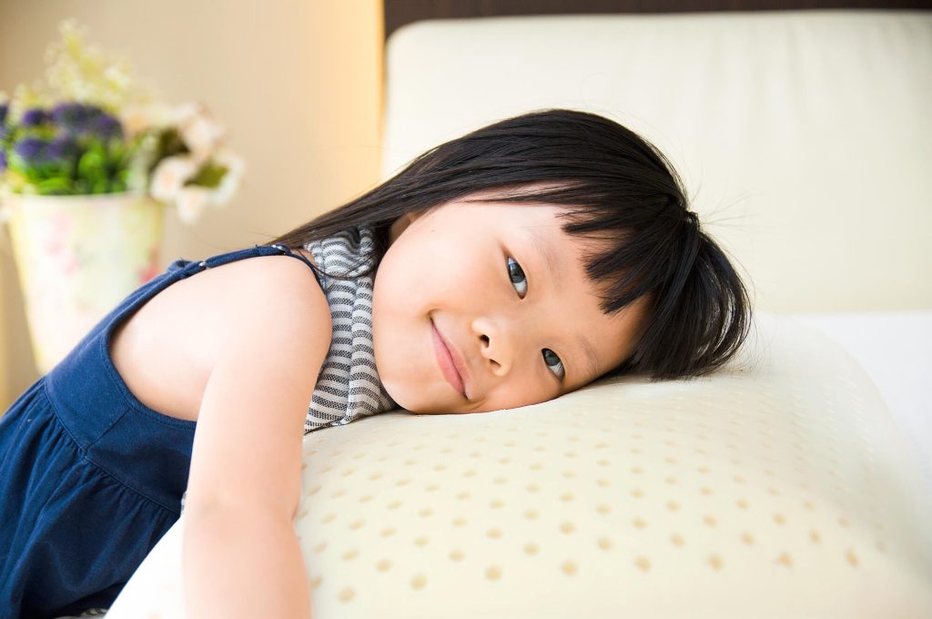 Young girl smiling, with her head on a latex pillow